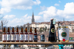 Acht Biere, eine Dose, eine zwei Liter Flasche und eine fünf Liter Dose aufgereiht vor der Aussicht auf die Berner Altstadt.
