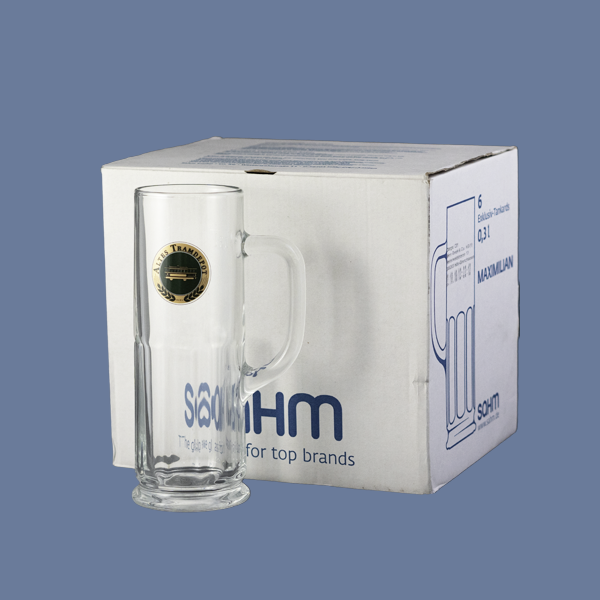 Im Vordergrund steht das Glas mit dem Tramdepot Logo drauf und im Hintergrund ist der 6er Karton, in dem die Gläser verpackt sind und geliefert werden.
