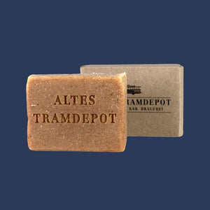Seife mit Schriftzug "Altes Tramdepot" eingestanzt. Im Hintergrund Kartonverpackung mit Tramdepot Logo drauf.